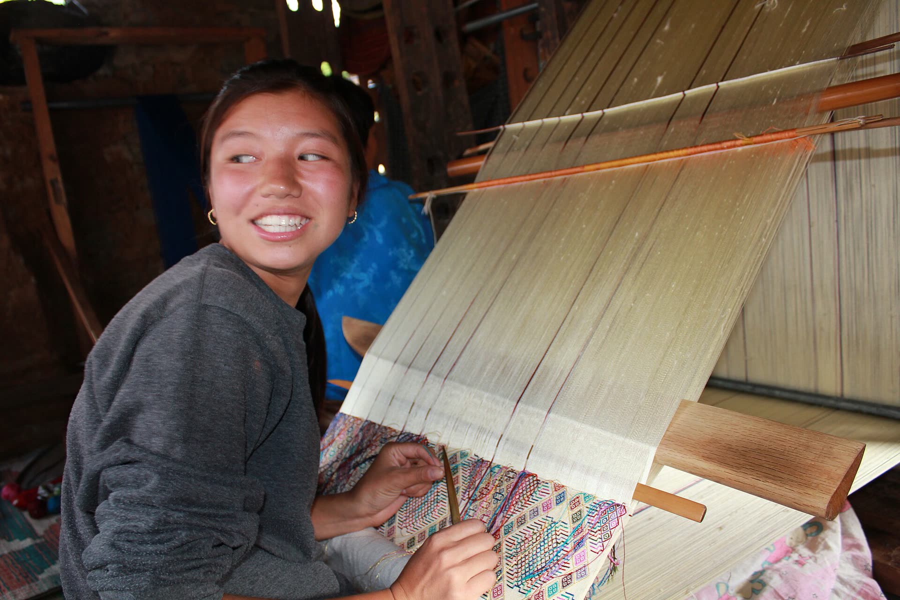 A weaver in Khoma village, eastern Bhutan, smiling at her loom